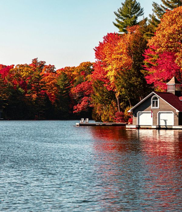 A little cottage sitting on the lake with the different colours of autumn trees in the backdrop.